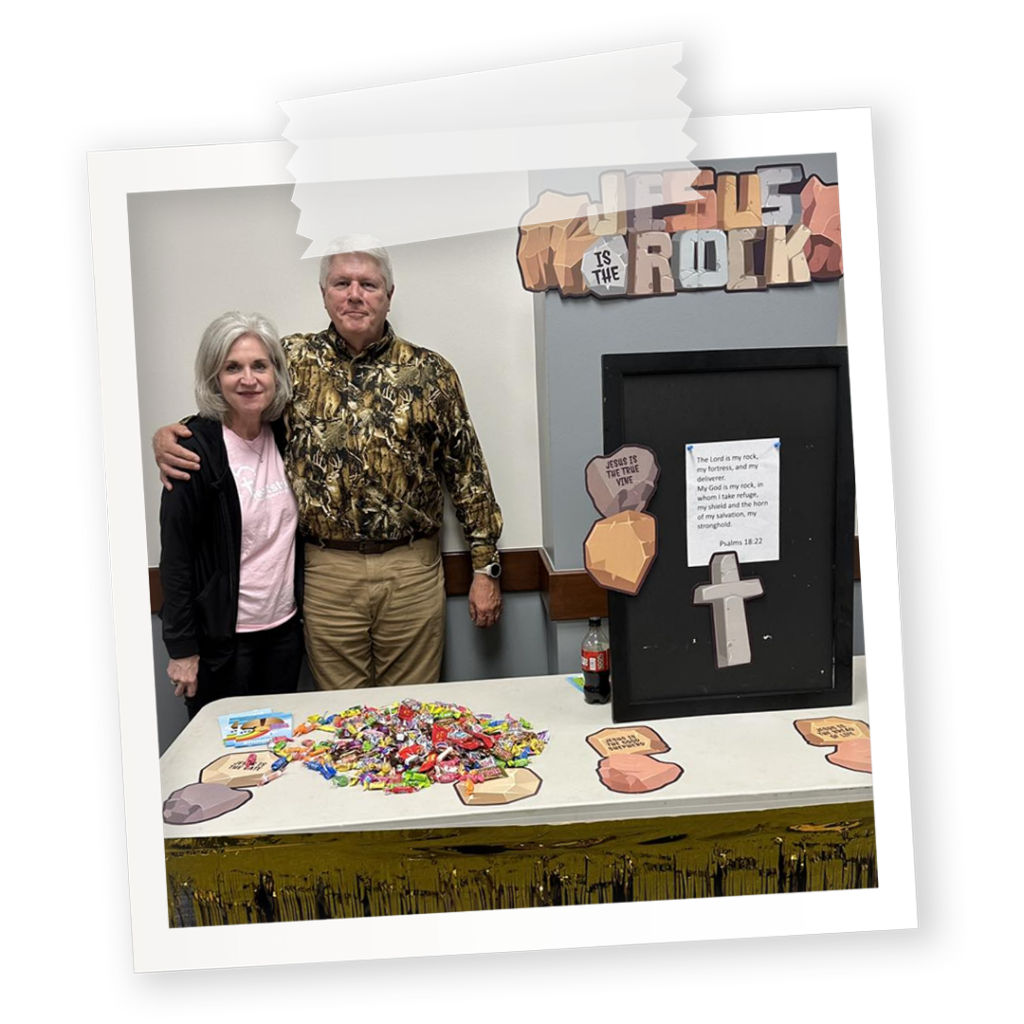 A church trunk-or-treat booth for Jesus is the Rock featuring a couple standing in front of a table with lots of paper rocks and candy.